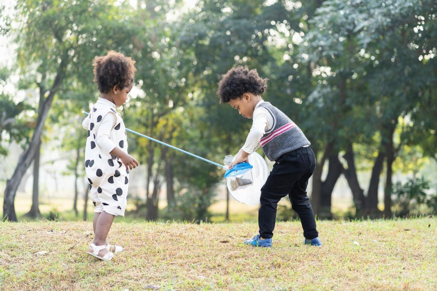 Two small children exploring a green park with a butterfly net, learning to care for nature